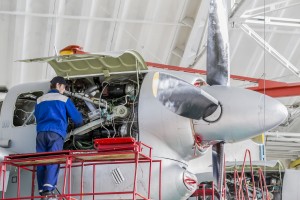 工程师航空厂修理喷气发动机在航空机库。飞机在重度维护下。在蓝色工作制服的技术员